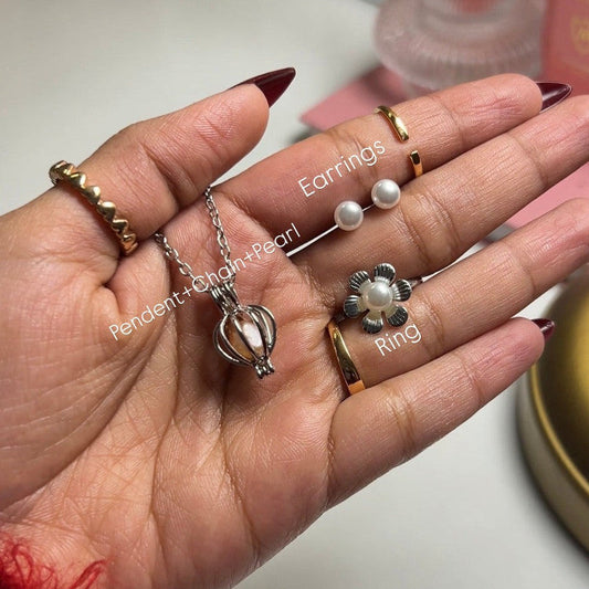 Hand holding jewelry including earrings, a pendant, and a ring on a light background.